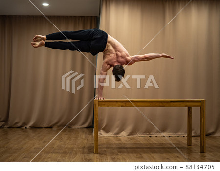 A muscular man keeps balance on one hand indoor. Concept of healthy lifestyle, yoga and handstand A muscular man keeps balance on one hand indoor. Concept of healthy lifestyle, yoga and handstand 88134705