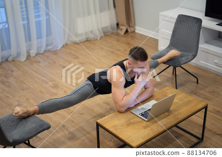 Flexible man work on laptop and doing leg-split at home. Concept of willpower, motivation and passion Flexible man work on laptop and doing leg-split at home. Concept of willpower, motivation and passion 88134706