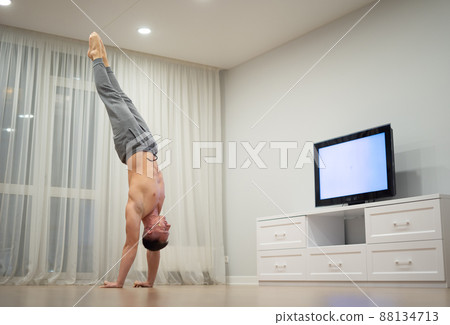 A man does handstand, keeps balance watching TV. Concept of originality, creativity and outstanding A man does handstand, keeps balance watching TV. Concept of originality, creativity and outstanding 88134713