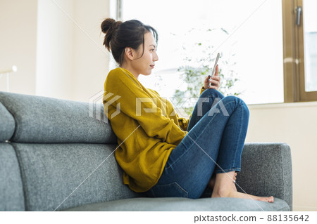 A woman looking at her smartphone on the sofa at home 88135642