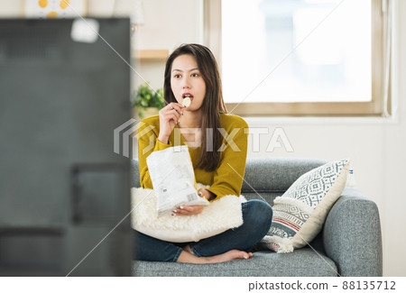 一個女人一邊吃甜食一邊看電視 88135712