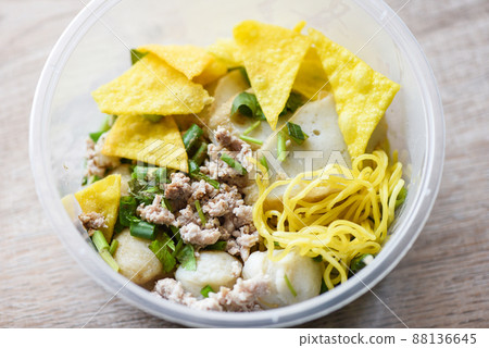 dry noodles pork balls fish balls and minced pork with crispy wontons and vegetable in plastic bowl on wooden table, top view Thai and China Asian food delivery concept 88136645