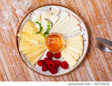 Slices of hard and soft cheeses on plate with raspberries and honey 88139426