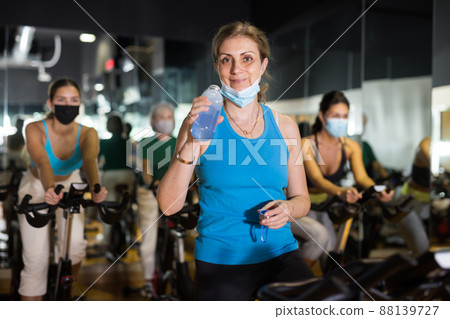 Adult woman in mask with fitness bike in gym Adult woman in mask with fitness bike in gym 88139727