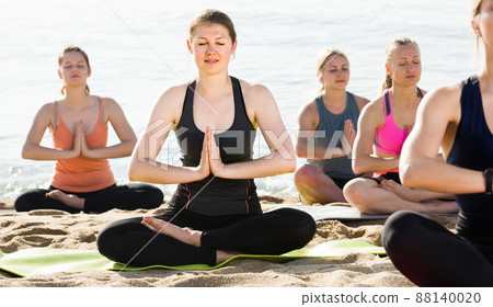 Sporty females meditating in yoga position Padmasana on seaside 88140020