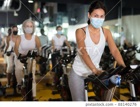Woman wearing mask riding bike in gym Woman wearing mask riding bike in gym 88140276