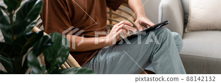 Technology Concept The male with his casual T-shirt and jeans sitting comfortably on the wooden chair and doing touchscreen for checking the web browser on the iPad 88142132