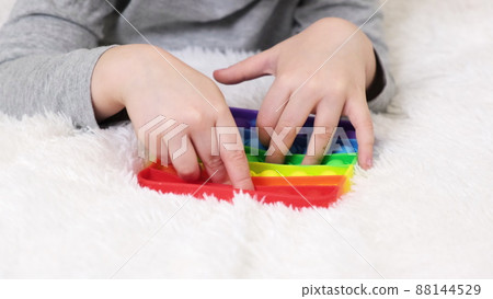Little boys hands are playing an educational game. Colorful antistress sensory toy fidget push pop it in toddler's hands. Antistress trendy pop it toy. Rainbow sensory fidget. New trendy silicone toy 88144529