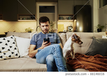 Man sit on sofa with dog and use smartphone Man sit on sofa with dog and use smartphone 88146016