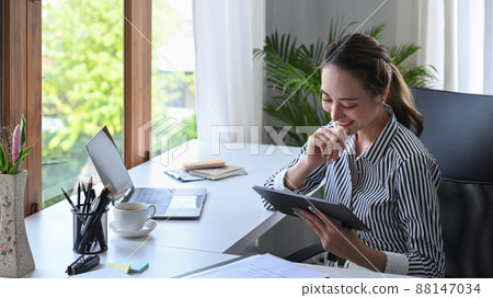 Young smiling female entrepreneur using digital tablet at contemporary workplace. 88147034