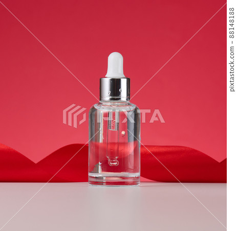 glass transparent white bottle with a pipette. Container for cosmetics, acids and oils on a red background 88148188