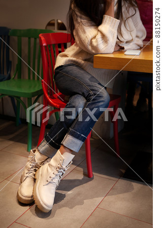 Close up details of women's fashion casual clothing. Legs in denim pants and high leather ankle boots with laces. Woman is sitting at table in cafe Close up details of women's fashion casual clothing. Legs in denim pants and high leather ankle boots with laces. Woman is sitting at table in cafe 88150274