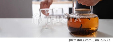 Hands hold a glass teapot and an empty cup, close-up 88150773