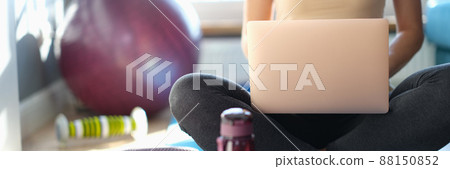 Woman sitting on floor with laptop, next to sports equipment Woman sitting on floor with laptop, next to sports equipment 88150852
