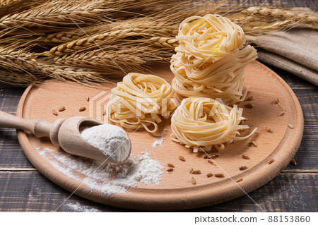 on a wooden cutting board tagliatelle noodles, sheaf of wheat, and flour, concept on a wooden cutting board tagliatelle noodles, sheaf of wheat, and flour, concept 88153860