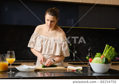 Pregnant woman cuts a cucumber into thin slices in the kitchen 88154750