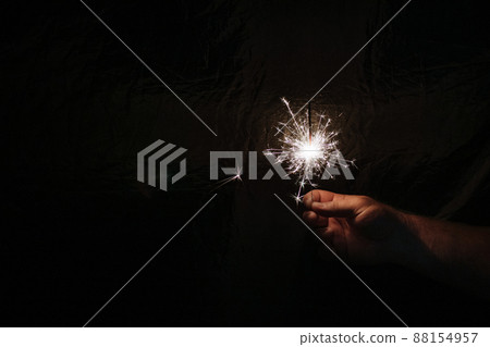 Hand with sparkler on dark background. Celebrating new year with sparkler. Hand holding sparkler on dark background. Christmas fun. New year concept Hand with sparkler on dark background. Celebrating new year with sparkler. Hand holding sparkler on dark background. Christmas fun. New year concept 88154957