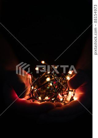 male hands holding a Christmas garland with lights on a dark background with copy space for text. Retro effect, close-up. Winter, postcard template. 88154973