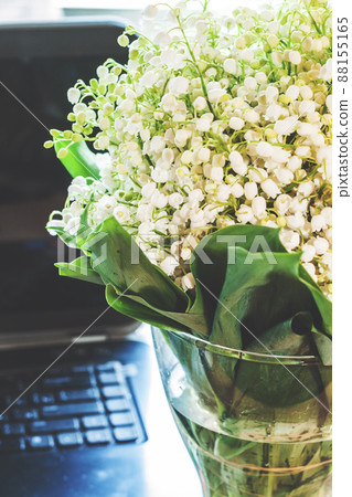 A woman's workplace, a bouquet of lilies of the valley in a vase near the laptop. With a retro vintage effect. 88155165