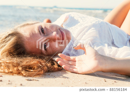 Young adult tanned blond girl lies on the sand on the beach near the sea and smiles. Young adult tanned blond girl lies on the sand on the beach near the sea and smiles. 88156184