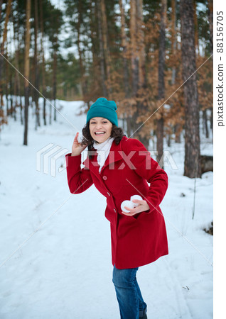 Attractive cheerful Caucasian woman in warm clothes playing snowballs, enjoying beautiful cold winter day in a snow covered forest. Winter active pastime concept. Travel, holidays, weekend, trip 88156705