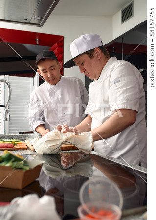 Two happy young asian chefs dressed in white uniform preparing traditional japanese sushi set in interior of modern professional kitchen. 88157755