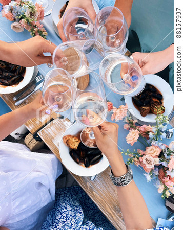 Group of friends cheering with glasses of white wine during picnic with mediterranean food outdoors 88157937