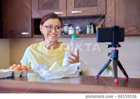 Woman cooking in kitchen talking online using video call on smartphone with tripod Woman cooking in kitchen talking online using video call on smartphone with tripod 88158336