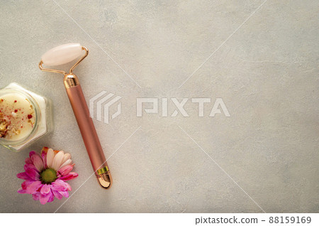 Pink quartz face roller with aroma candle, and flower on grey background. Minimal beauty flatlay with copy space 88159169