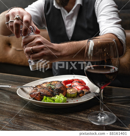 Pork steak with grilled vegetables is peppered by a man, having lunch in a restaurant Pork steak with grilled vegetables is peppered by a man, having lunch in a restaurant 88161401