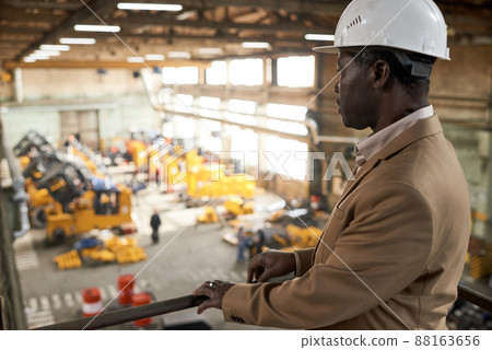 Serious African engineer in work helmet standing on balcony and watching for the work of machines in factory Serious African engineer in work helmet standing on balcony and watching for the work of machines in factory 88163656