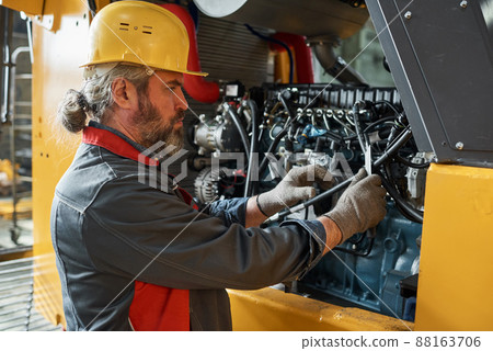 Mature bearded mechanic in uniform examining the machine and repairing it in factory 88163706