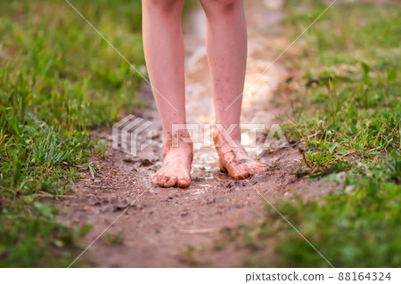 Barefoot girl walks through a puddles of water after the summer rain. Barefoot girl walks through a puddles of water after the summer rain. 88164324