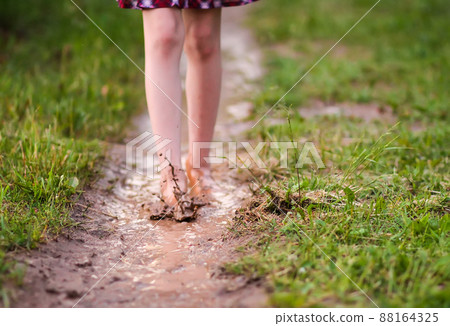 Barefoot girl walks through a puddles of water after the summer rain. 88164325