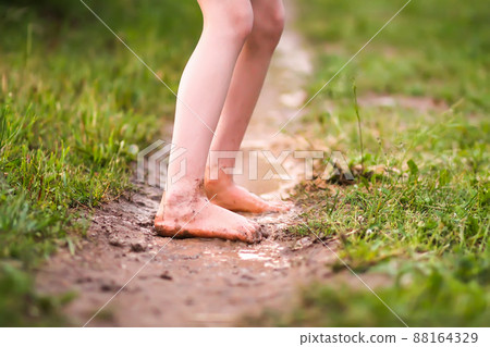 Barefoot girl walks through a puddles of water after the summer rain. 88164329