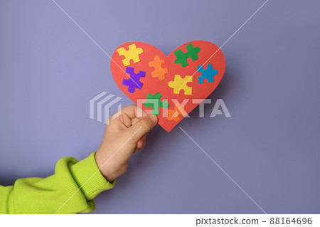 A big red heart with details of colored puzzles inside in a child's hand there is a symbol of autism. World Autism Day A big red heart with details of colored puzzles inside in a child's hand there is a symbol of autism. World Autism Day 88164696