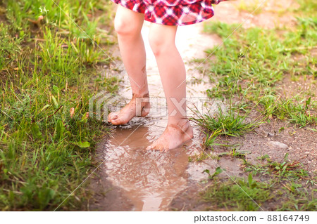 Barefoot girl walks through a puddles of water after the summer rain. 88164749