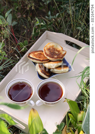 Tea in country style in summer garden in the village. Two cups of black tea and cupcakes on wooden tray in sunlight. 88164794