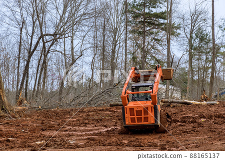 Excavator uprooting trees on land in bulldozer clearing land from trees, roots and branches 88165137