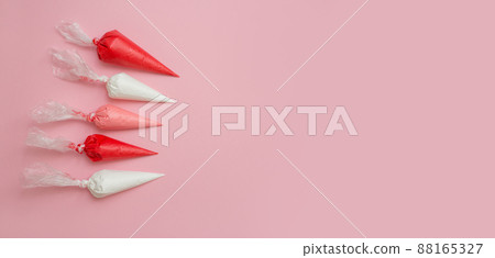 Colorful glazing in icing bags to cover gingerbread, cakes and cookies on a pink background. Set for decorating desserts. Cake decorating tools. Banner. Confectionery concept. 88165327