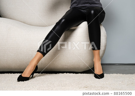 Cropped image of woman in beige pantyhose and black trousers sitting on couch 88165500