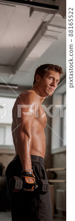 Strong muscular man holding a dumbbell in the gym Strong muscular man holding a dumbbell in the gym 88165522