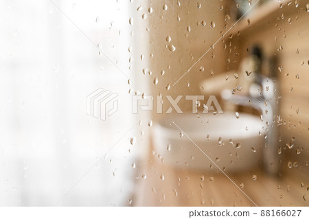 Wet glass shower door in hotel bathroom with blured window, sink and faucet Wet glass shower door in hotel bathroom with blured window, sink and faucet 88166027