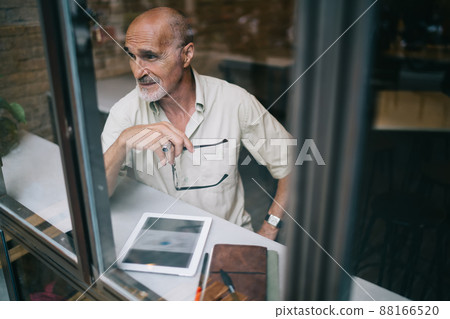 Window view of old Caucaisan journalist with optical glasses in hand thoughtful looking away 88166520