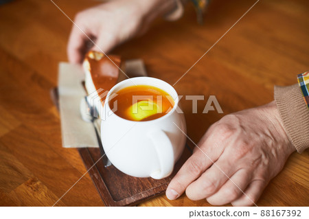 A cup of tea and dessert in the hands of a young man. Front view. 88167392