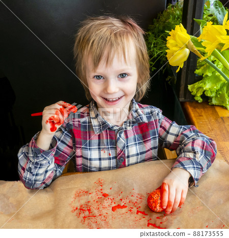The child preparing for Easter. Paint eggs. Red paint egg. 88173555