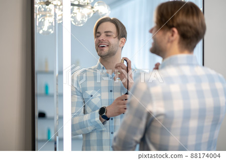 Happy and smiling man spraying perfume and looking contented Happy and smiling man spraying perfume and looking contented 88174004