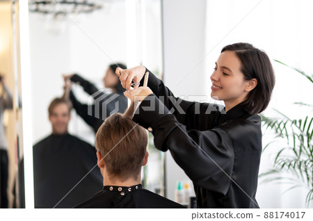 Dark-haired hairdresser working on a stylish haircut Dark-haired hairdresser working on a stylish haircut 88174017