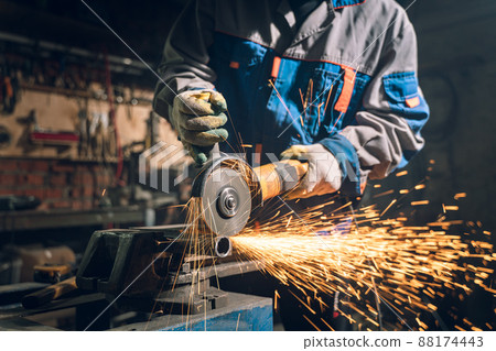 Locksmith in special clothes and goggles works in production. Metal processing with angle grinder. Sparks in metalworking 88174443