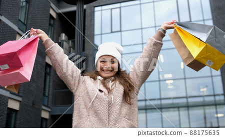 Happy girl raises hands and holds the multi-colored shopping bags in the street Happy girl raises hands and holds the multi-colored shopping bags in the street 88175635
